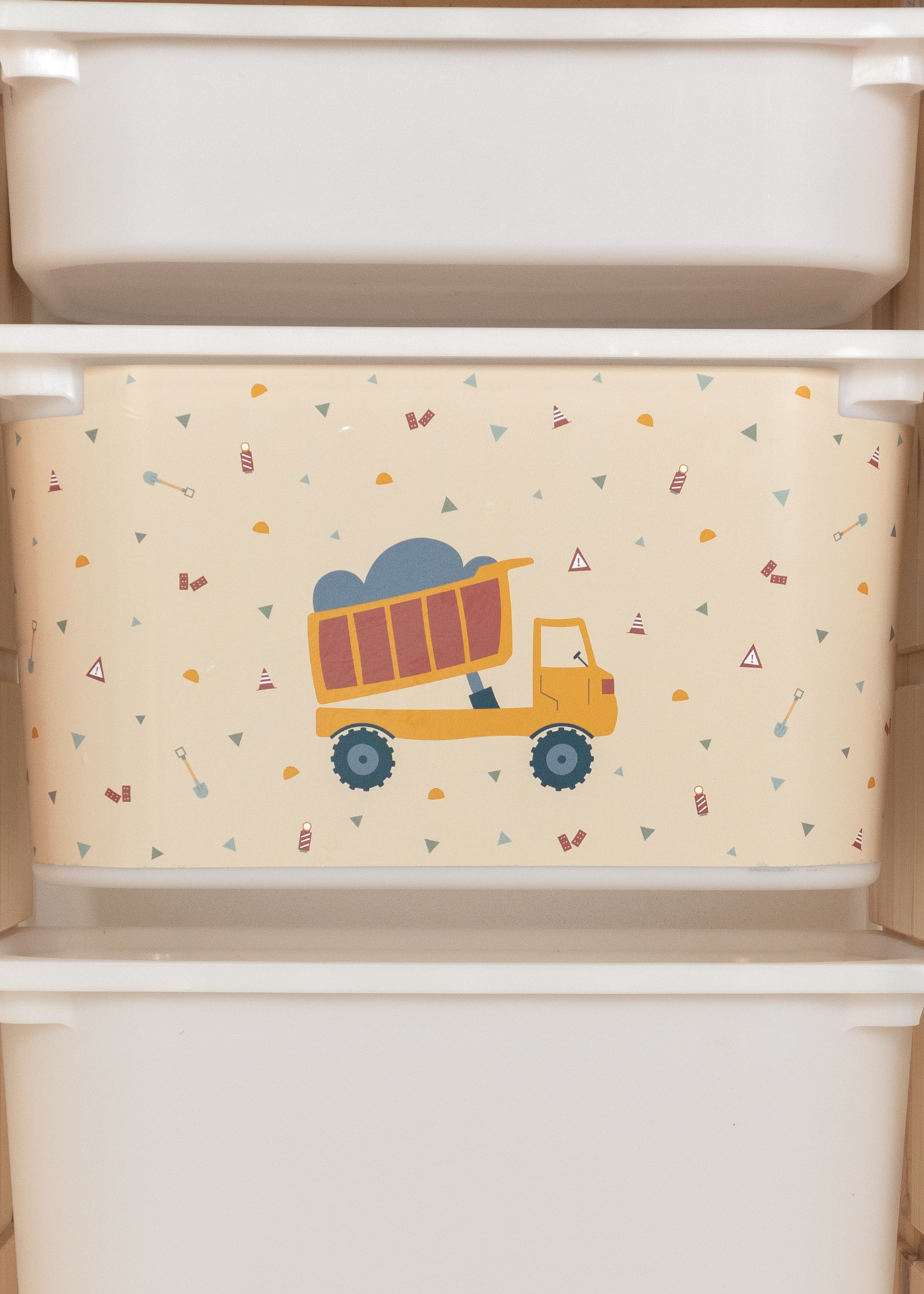 Kipplader-Motiv auf beiger Box im IKEA TROFAST Regal für Kinder.