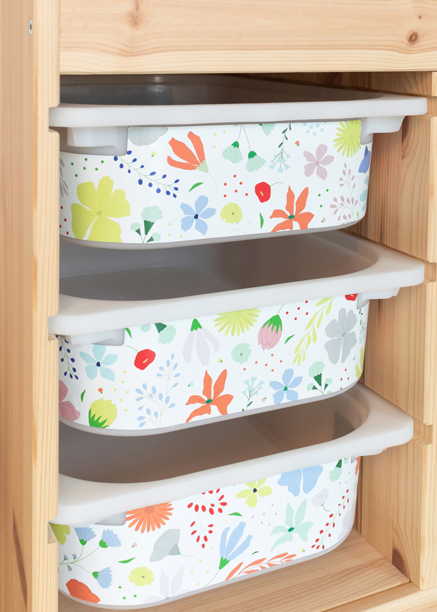 Drei IKEA TROFAST Boxen mit Blumenmuster Ein IKEA TROFAST Regal steht in einem Raum, geschmückt mit einer Möbelfolie im Blumenmuster