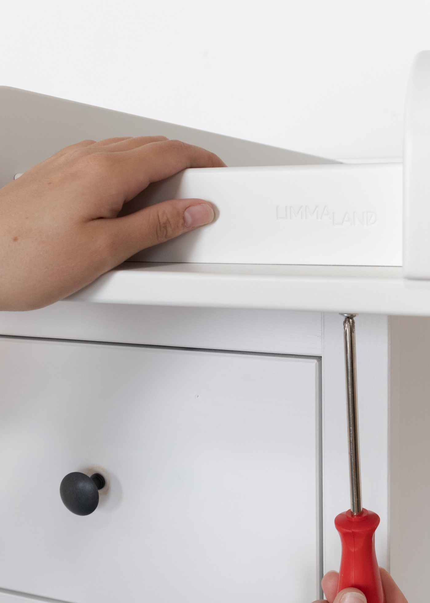 Wickelaufsatz an IKEA Hemnes anschrauben Eine Person schraubt den Limmaland WIckelaufsatz an die IKEA Hemnes Kommode