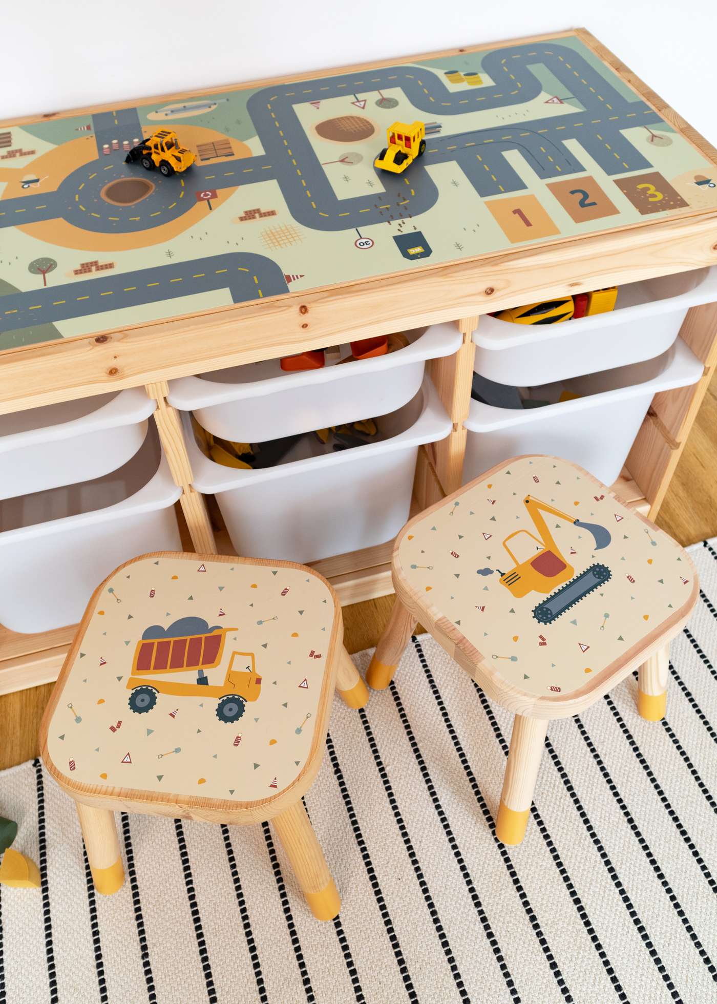 Zwei IKEA FLISAT Kinderhocker mit Klebfolien von Limmaland mit Baustellenmotiven stehen vor einem IKEA Trofast Regal mit Limmaland Spielstraße