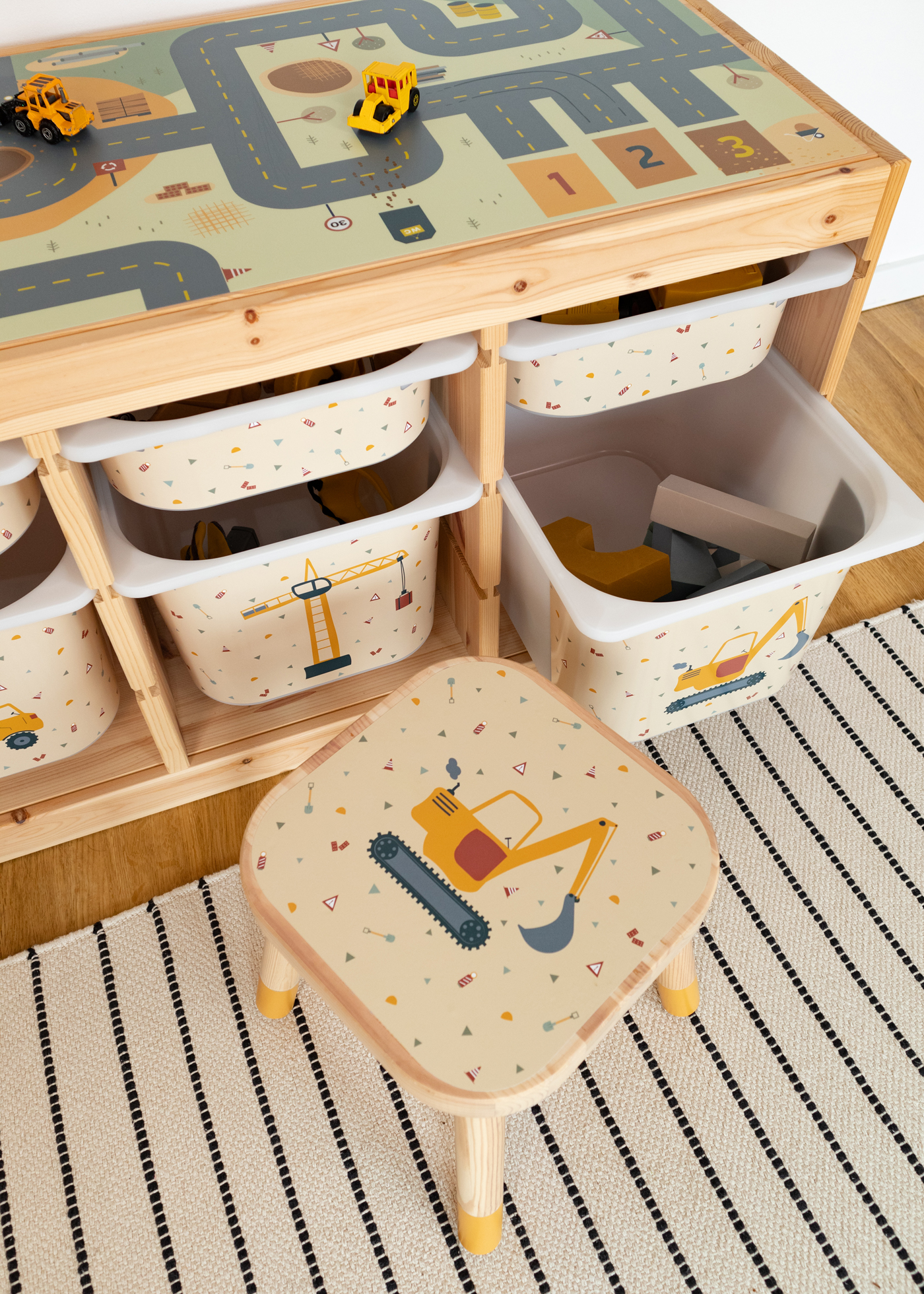 Ein IKEA FLISAT Kinderhocker mit Zubehör und Klebefolien von Limmaland mit Bagger Motiv vor einem Trofast Regal
