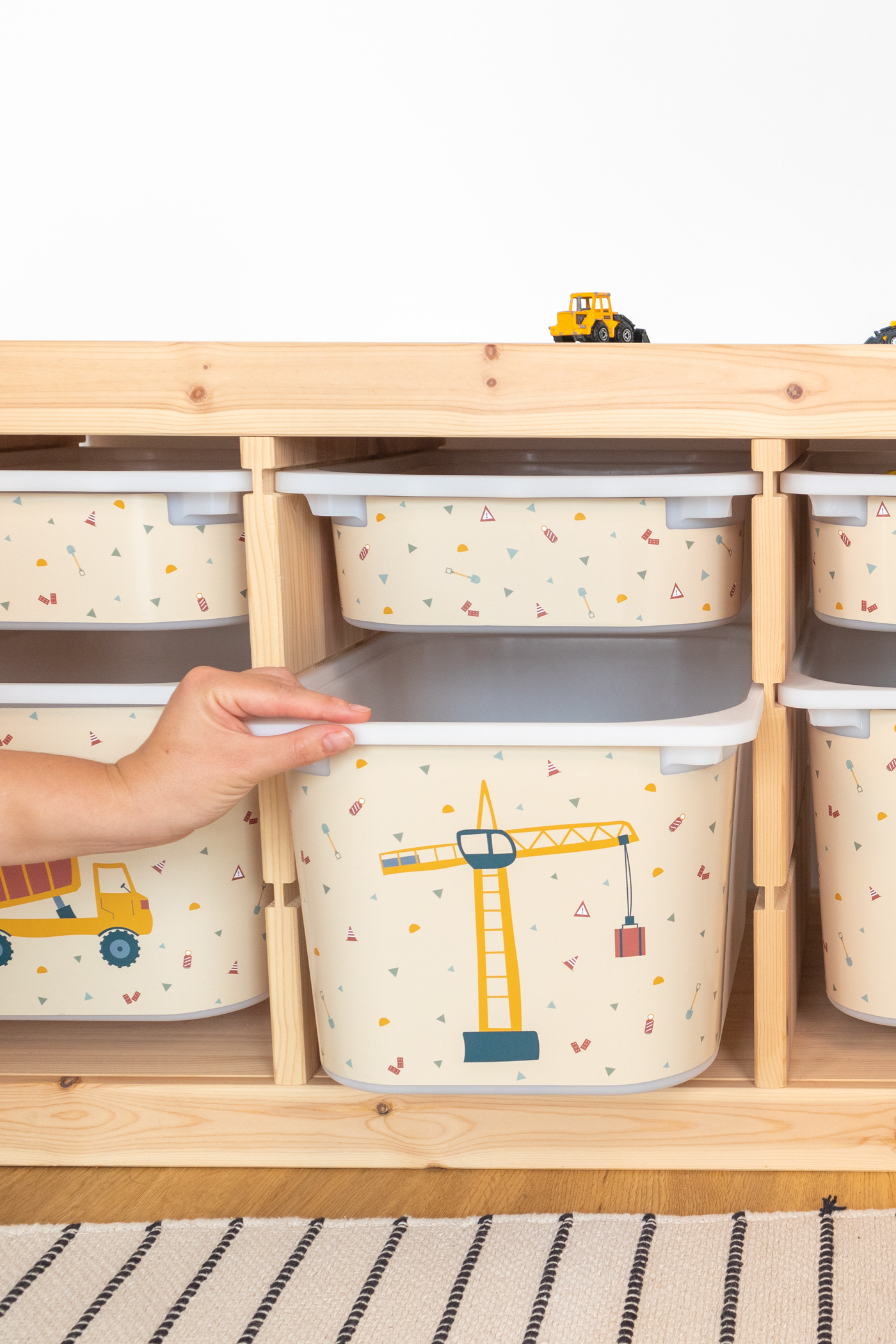 Aufbewahrungslösung im IKEA TROFAST Regal mit einer beige Box, die Bagger, Kran und Kipplader zeigt, passend für das Kinderzimmer.