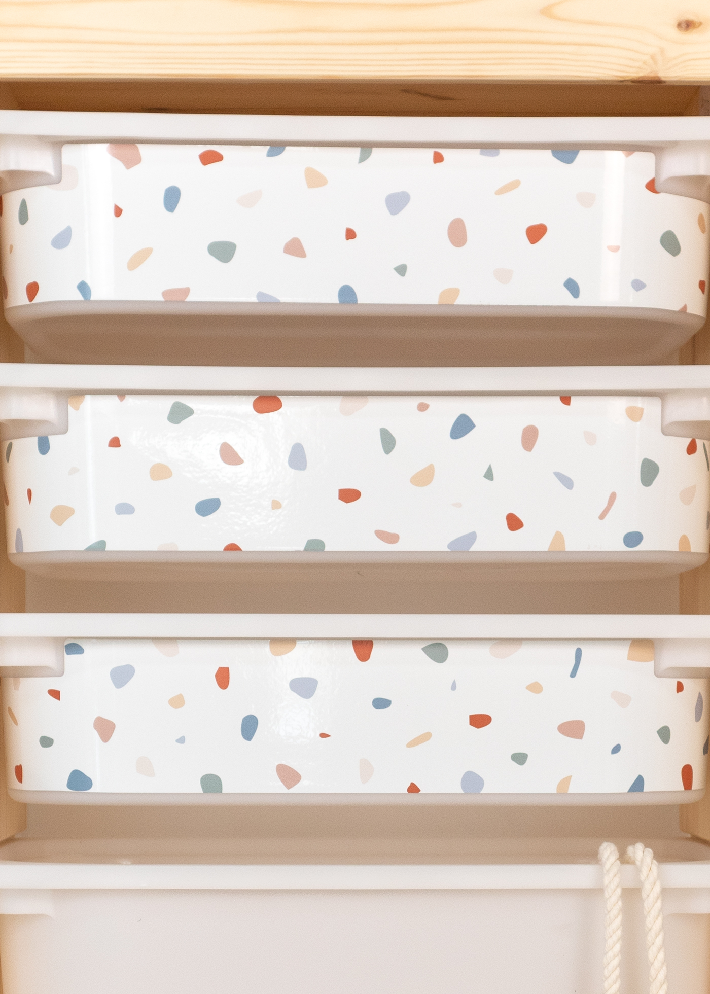 Aufbewahrungsbox im IKEA TROFAST Regal, dekoriert mit einer Klebefolie im bunten Terrazzo-Muster.