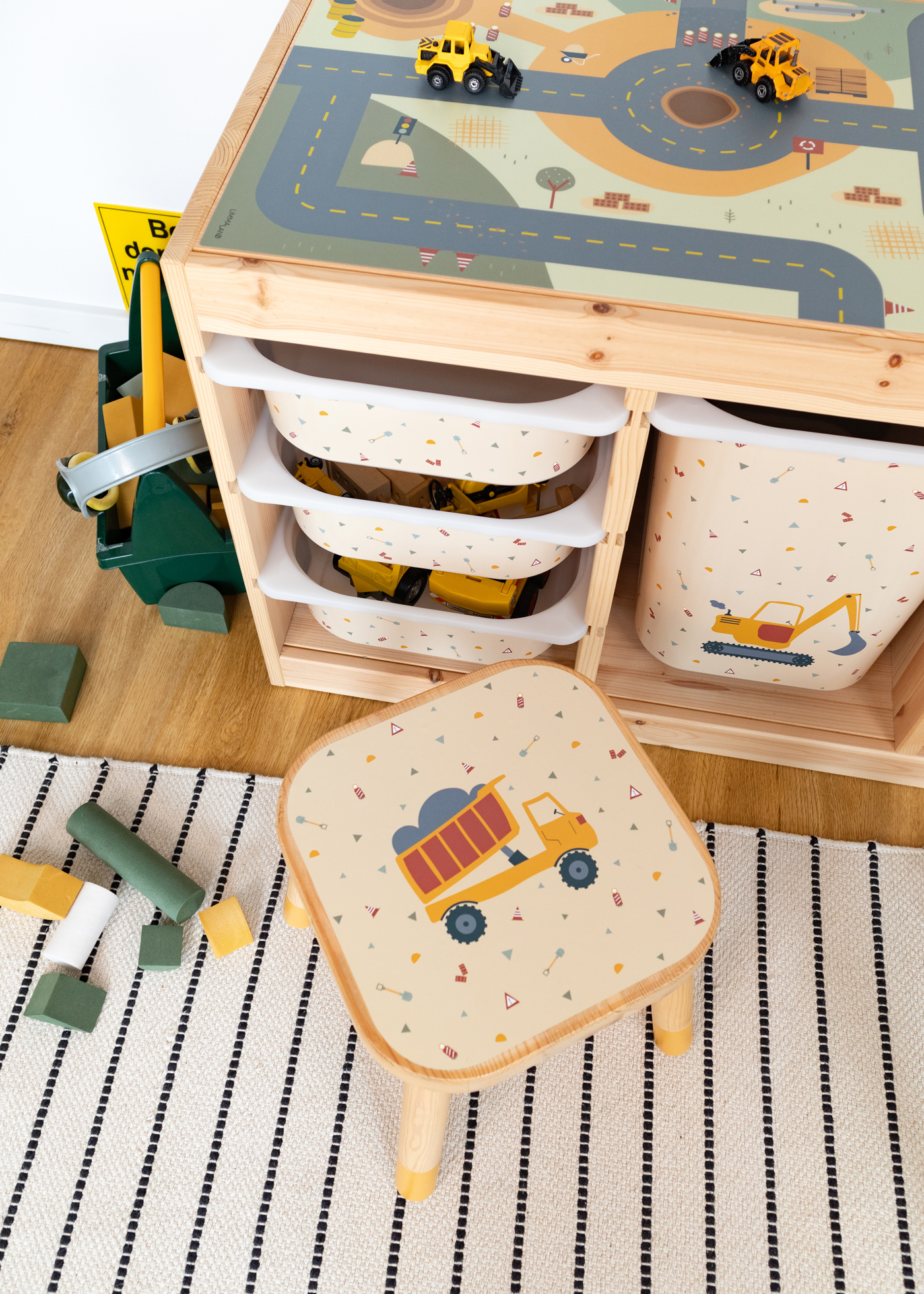 Ein IKEA FLISAT Kinderhocker mit Zubehör und Klebefolien von Limmaland mit Kipplader Motiv vor einem Trofast Regal