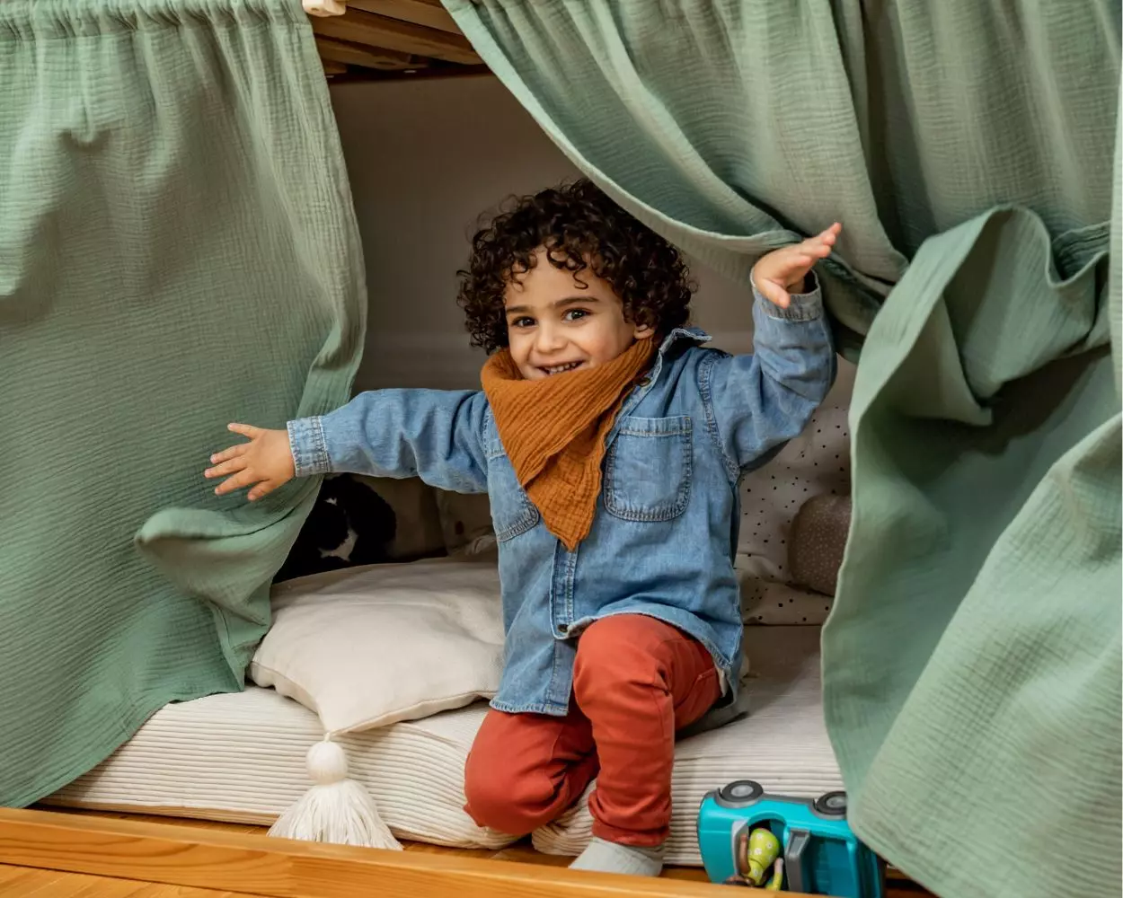 Ein Junge sitzt unter seinem Ikea-KURA-Hochbett und öffnet die Vorhänge
